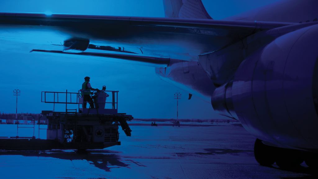 A photo with a blue overlay of an airport worker working on a plane