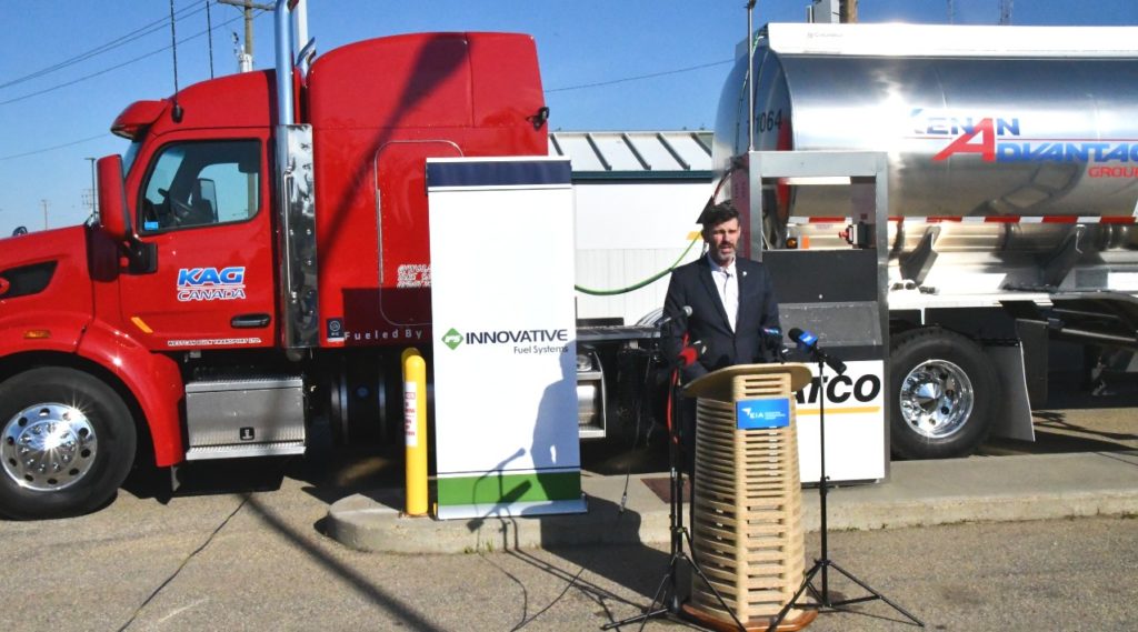 City of Edmonton Mayor Don Iveson standing at the podium outdoors in front of a red semi to congratulate Innovative Fuel Systems, KAG Canada and Edmonton International Airport for the development and use of technology reducing emissions in the truck transport industry.