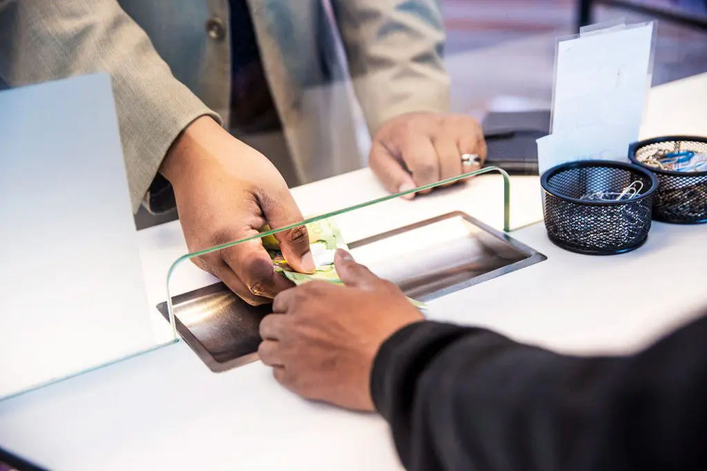 Photo d'un client échangeant des devises avec un préposé à travers une vitre de protection - International Currency Exchange