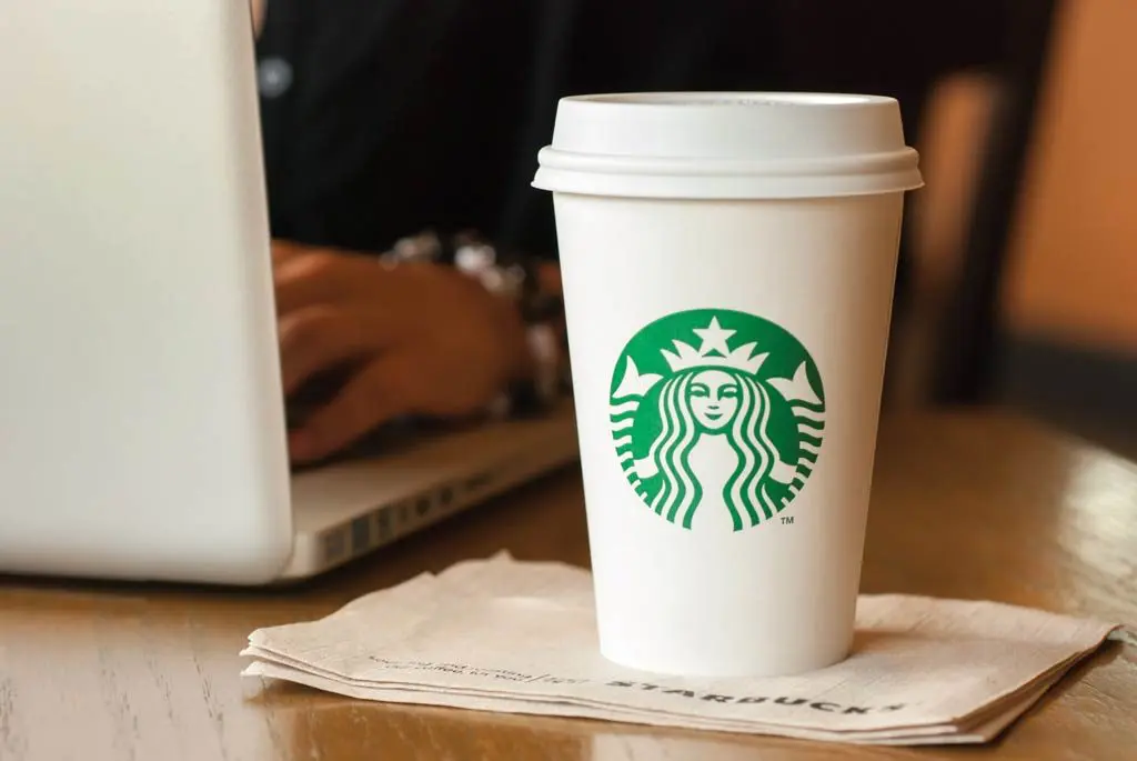 Photograph of customer working on laptop while enjoying a Starbucks coffee